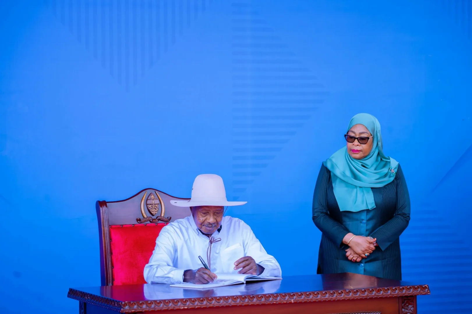 Museveni signs the visitors book as Samia looks on